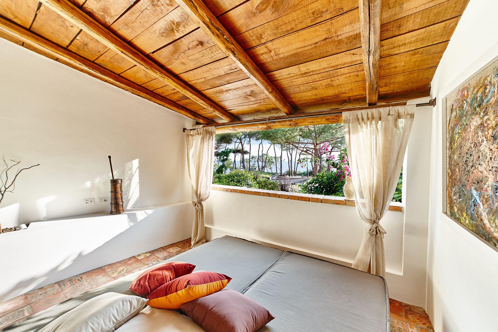 Una habitación con cama, ventana con cortinas, vistas a árboles y flores, y techo de madera.