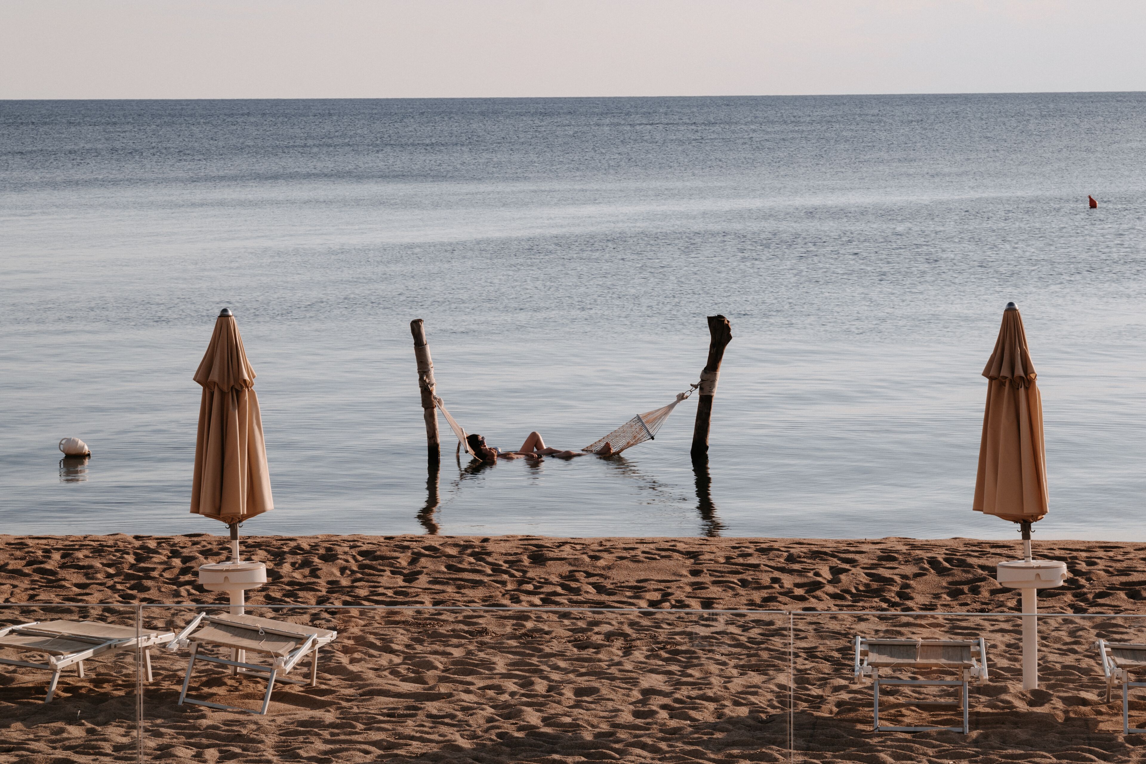 A beach with two umbrellas, a hammock, and lounge chairs.