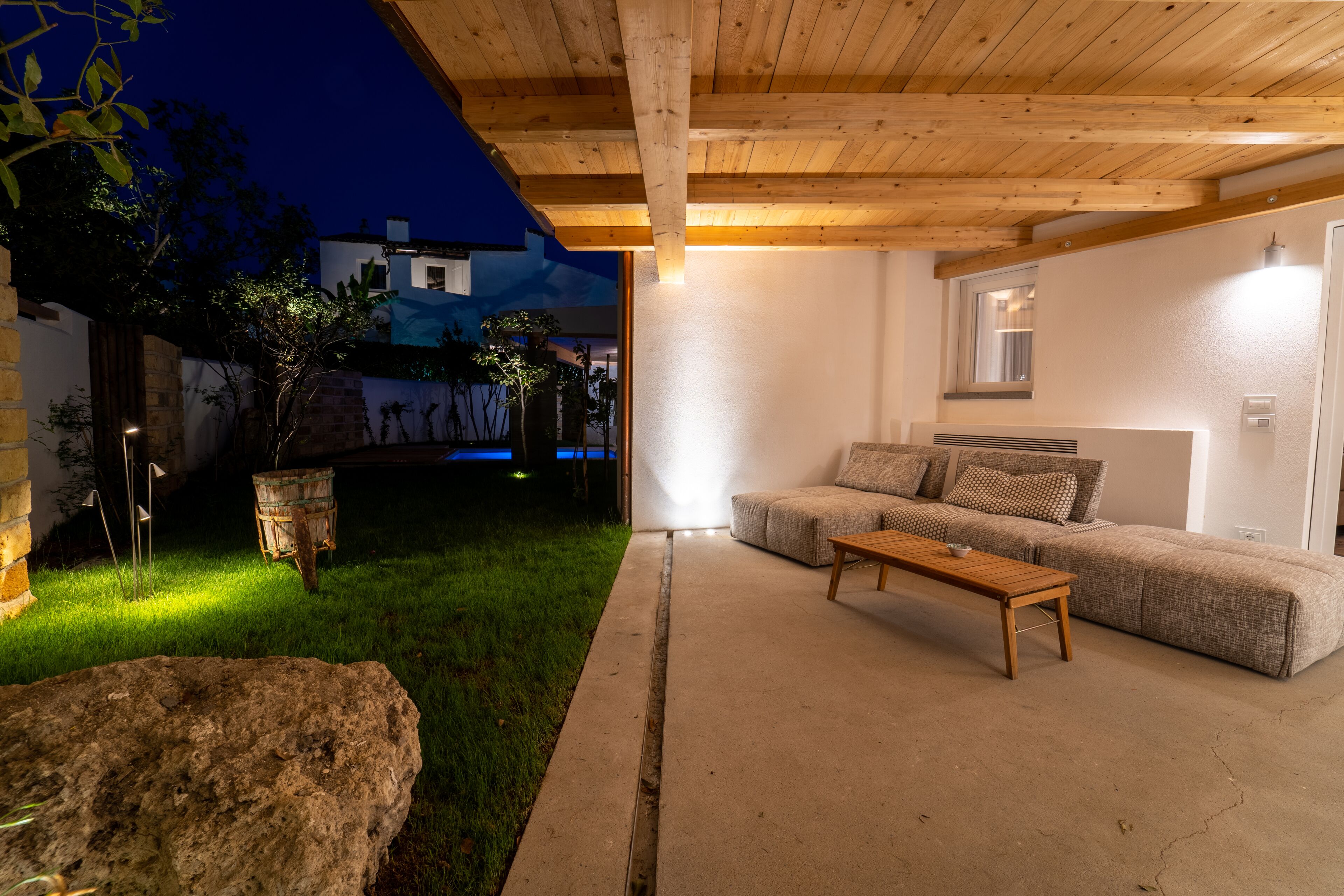 An outdoor living area with a wooden ceiling, a concrete floor, a sofa set, and a stone planter.