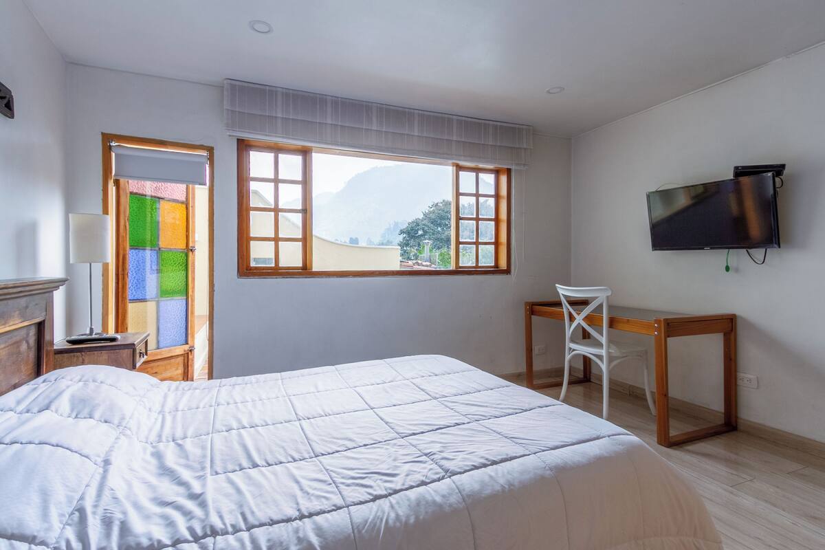 Une chambre à coucher comprenant un lit, un bureau, une chaise, un téléviseur et une fenêtre donnant sur les montagnes.