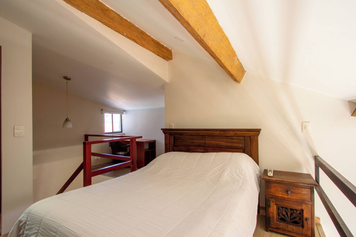 Une chambre à coucher avec un lit en bois, une table de chevet, un bureau et une fenêtre.