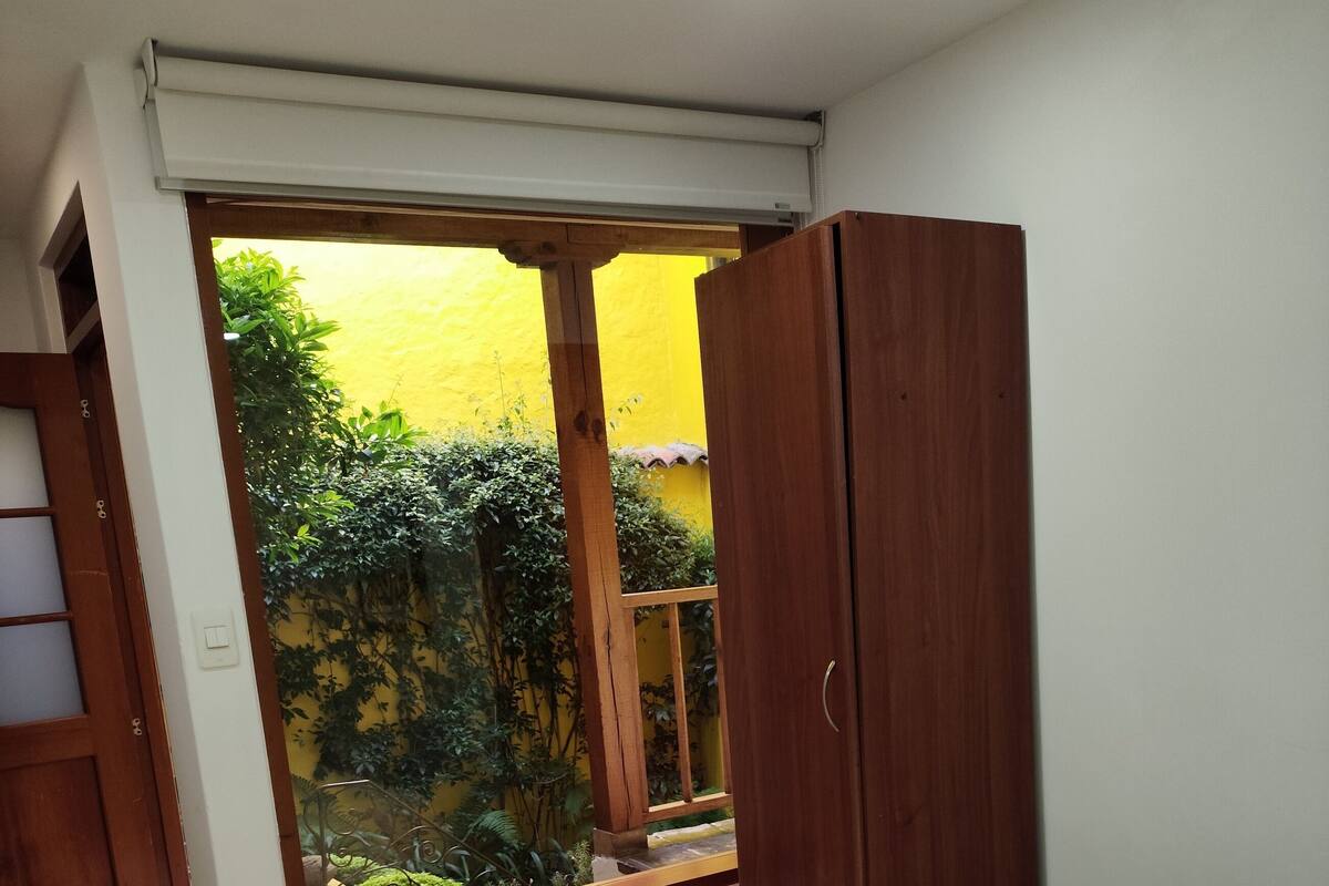 Une chambre avec une grande fenêtre, une armoire en bois et un lit doté d’un matelas blanc.