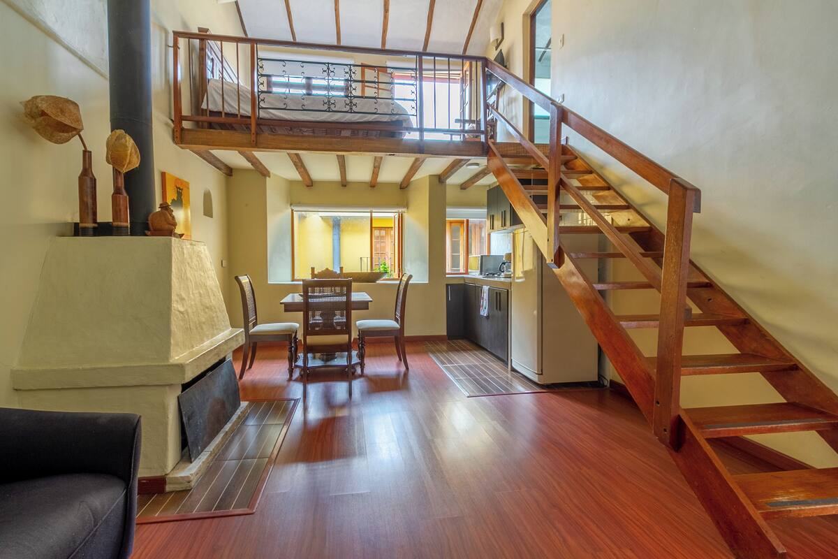Un vaste espace de vie agrémenté d’un escalier en bois, d’une table à manger avec des chaises et d’une cheminée.