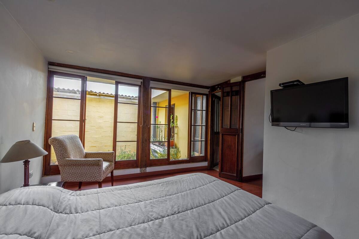 Une chambre avec un grand lit, une chaise, une télévision et une porte-fenêtre coulissante donnant sur un balcon.