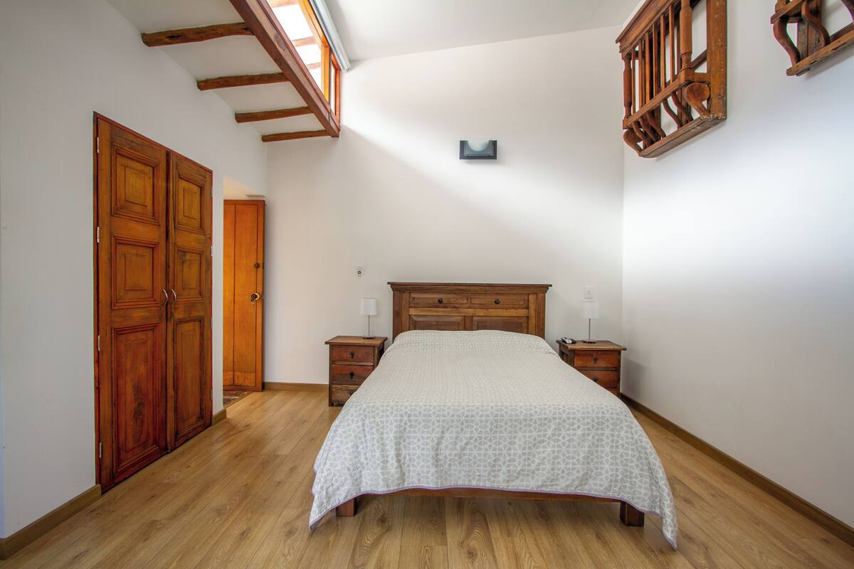 Une chambre à coucher avec un lit en bois, deux tables de chevet, une commode, une armoire et un puits de lumière.