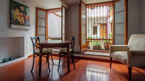 A room with a wooden dining table, chairs, a cushioned armchair, a painting on the wall, and a view through a shoji screen door.