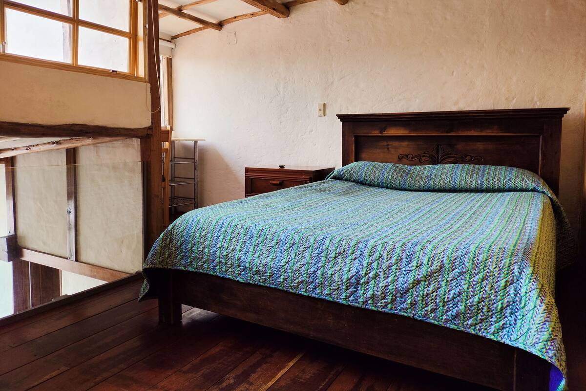 Une chambre avec un lit en bois, une échelle en bois et une fenêtre.
