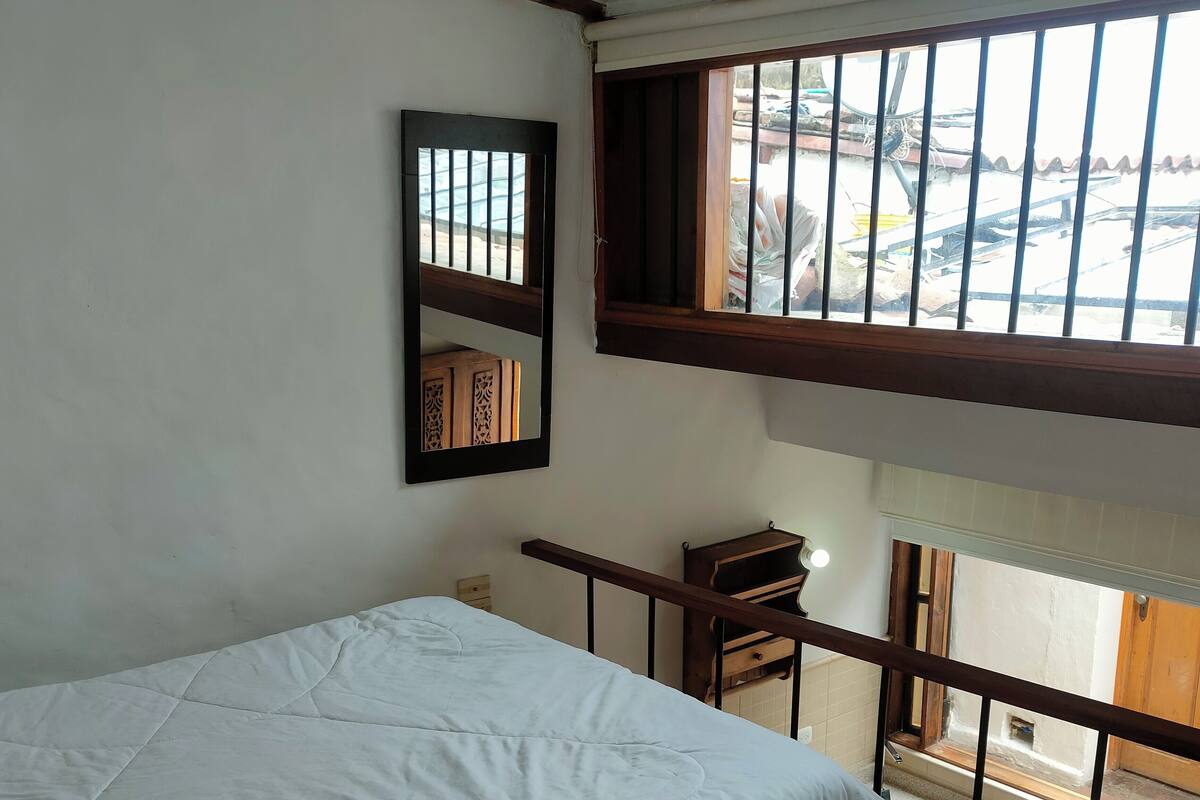 Une chambre à coucher avec un lit, un bureau en bois, un miroir et une fenêtre donnant sur l’extérieur.