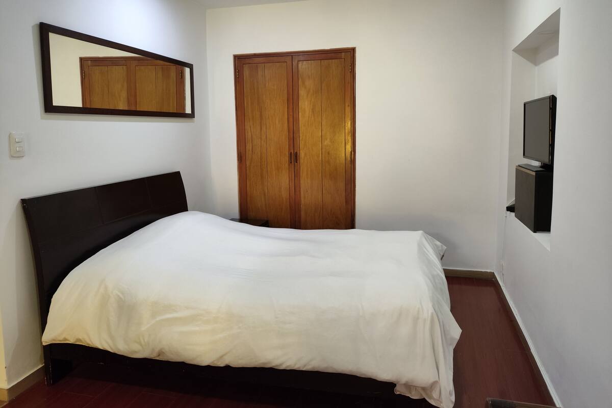 Une chambre à coucher avec un lit, une armoire, un miroir et un téléviseur.