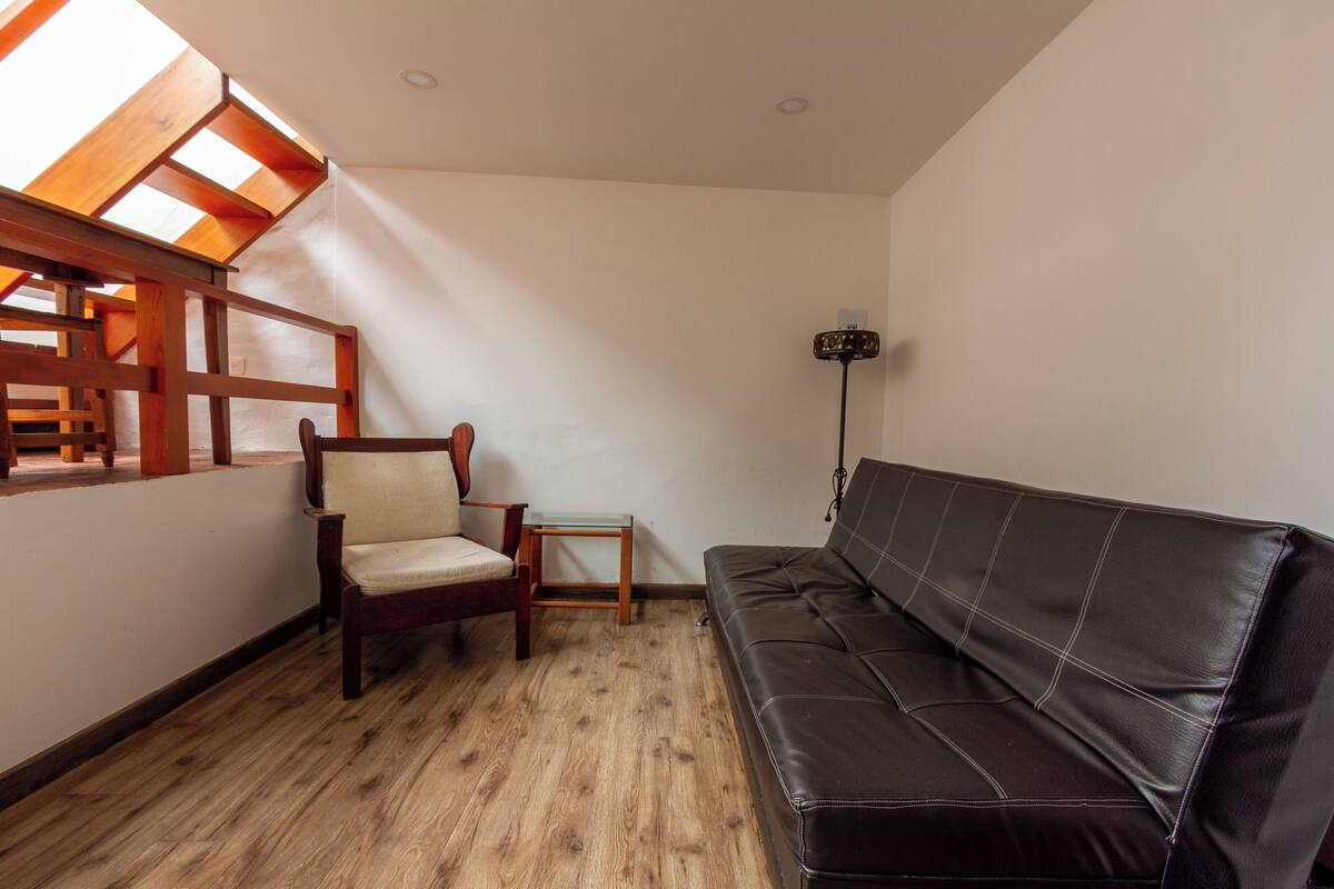 Une pièce avec un plancher en bois, un canapé en cuir noir, une chaise en bois, une petite table et un lampadaire.
