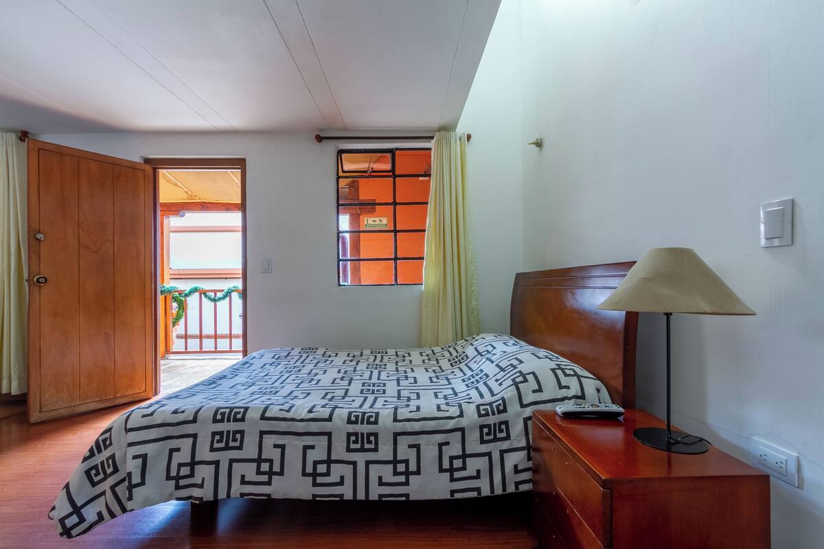 Une chambre à coucher avec un lit en bois, une table de chevet, une lampe et une fenêtre avec des rideaux.