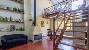 A spacious living area with a sofa, wooden staircase, and shelves with various bottles.