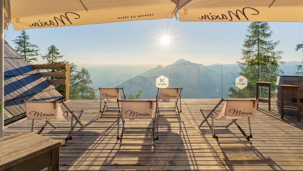 Una terraza con cuatro sillones de descanso etiquetados como "Maxim", una mesa de madera y vistas a las montañas.