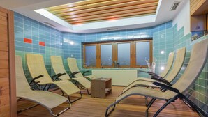 Una sala de sauna con suelo de madera, varias sillas reclinables, una mesita de madera y un ventanal con paneles de vidrio esmerilado.