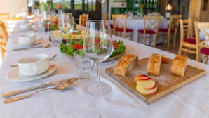 Una mesa de comedor dispuesta con mantel blanco, copas de vino, cubiertos, una cesta de pan y un plato de rodajas de manzana.
