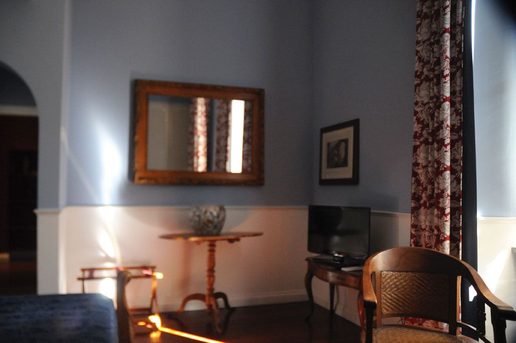 Una habitación con cama, una silla, una mesita, un espejo y una televisión.