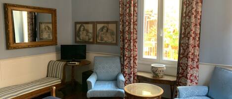 A room with a bed, two armchairs, a small table, a television, and a window with curtains.