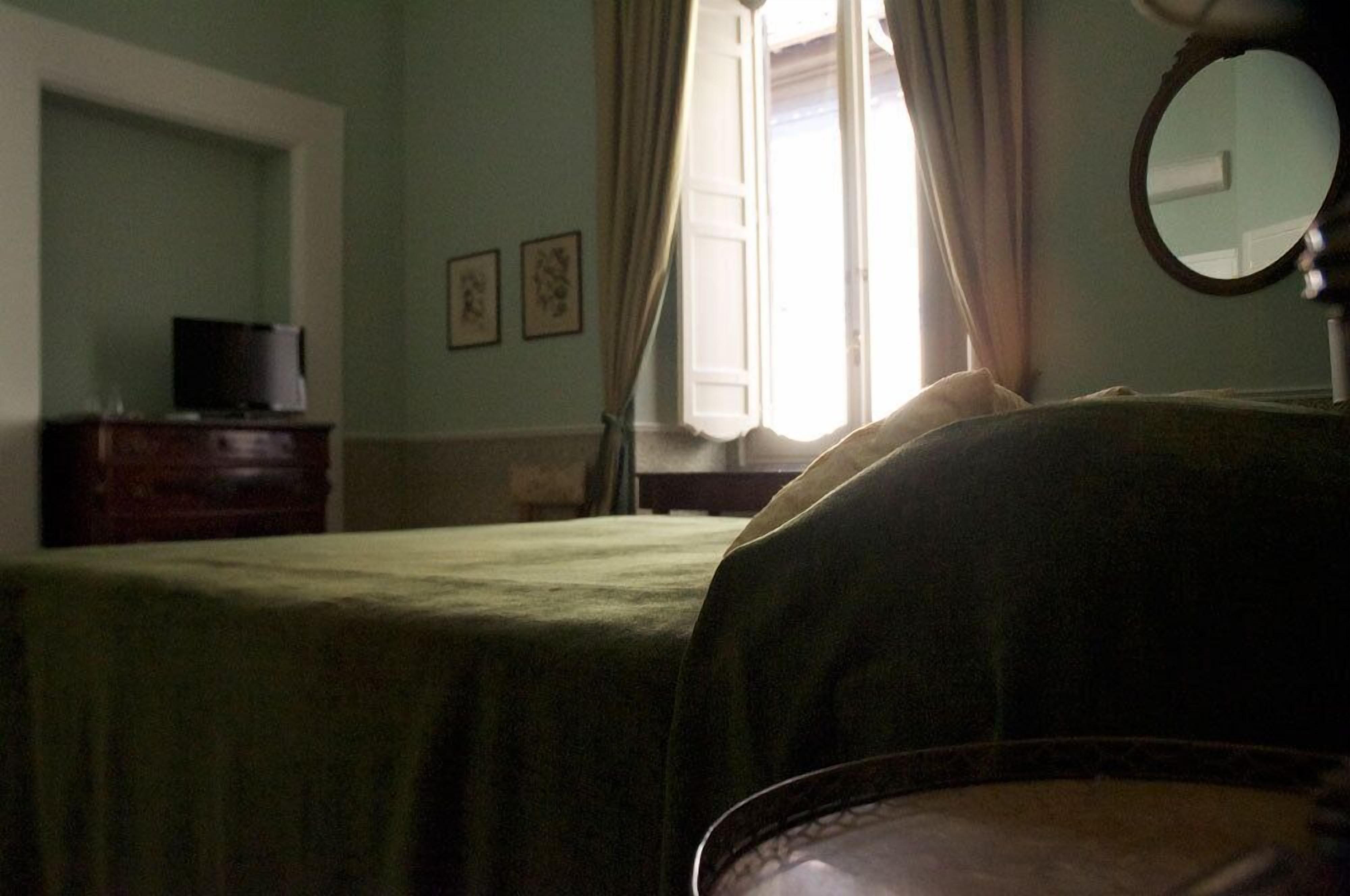 A room with a bed, a dresser, a mirror, and a window with curtains.
