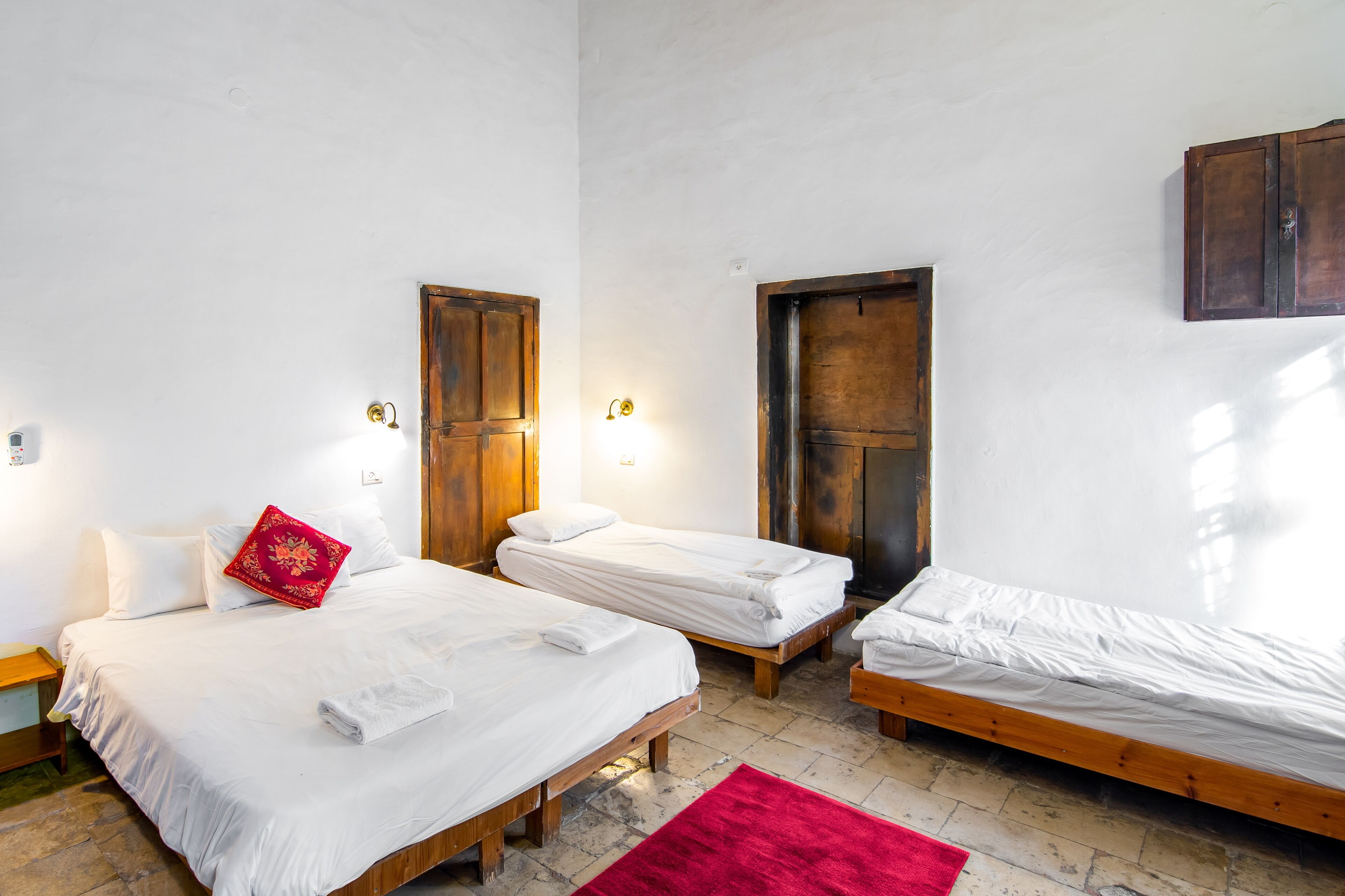 A room with three wooden beds, white bedding, and a red rug.