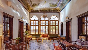 A spacious room with large arched windows, a chandelier, and a mix of wooden and upholstered furniture. - Fauzi Azar by Abraham (Nazareth)