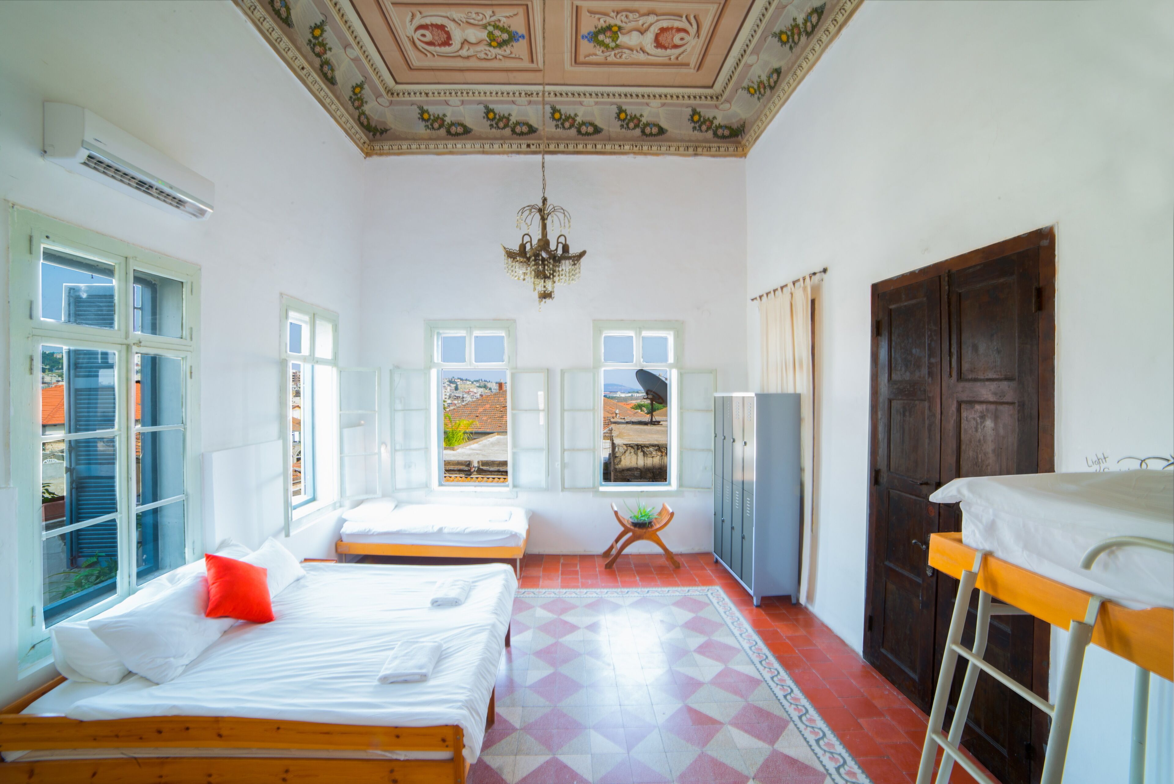 Quarto com duas camas, um candelabro, um guarda-roupa e vista para o exterior.