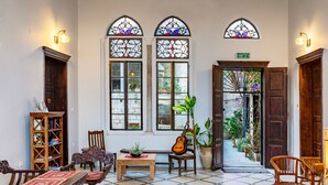 A room with a tiled floor, wooden furniture, a guitar, a bookshelf, and stained glass windows. - Fauzi Azar by Abraham (Nazareth)