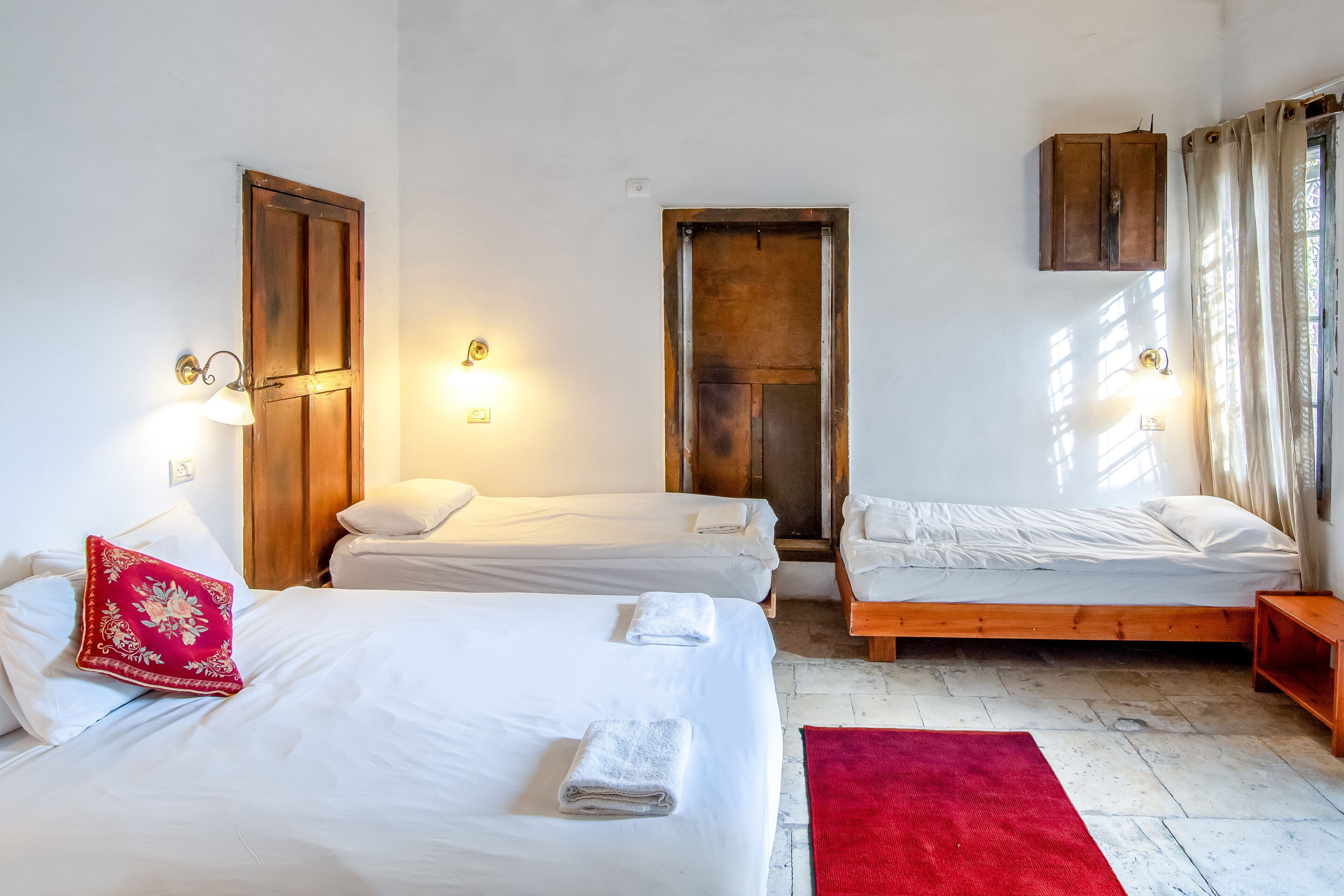 Une pièce avec trois lits, un tapis rouge et des portes en bois.