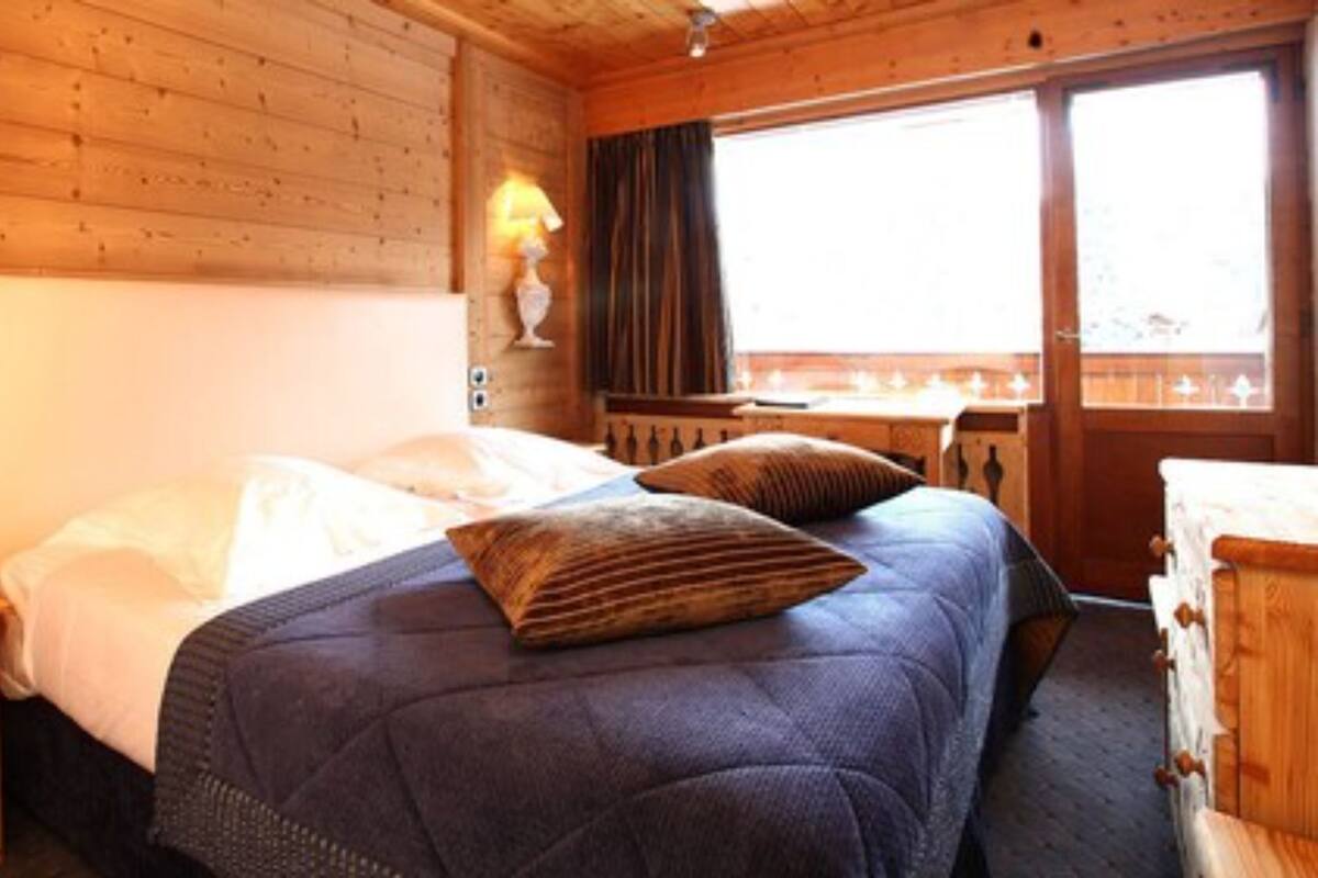 Une pièce en bois avec un lit, une table de chevet, une commode et une fenêtre avec des rideaux.