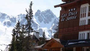 A mountain lodge named "Les Ducs de Savoie" with a wooden exterior and a view of snow-capped mountains in the background.