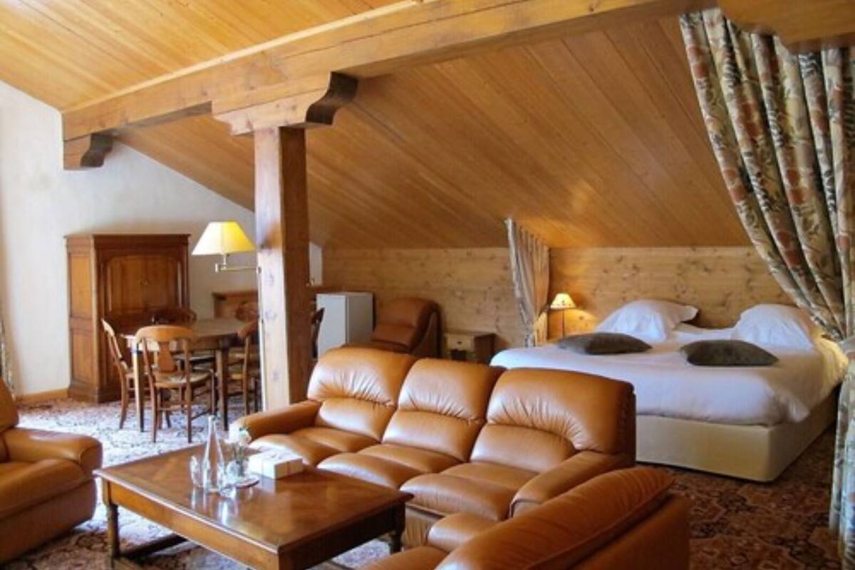 Une pièce chaleureuse avec un plafond en bois, un lit avec une literie blanche, un canapé en cuir, une table basse en bois et un bureau avec une lampe.