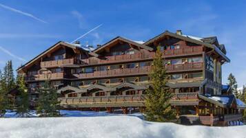Ein mehrstöckiges Chalet mit Balkonen und einer Skipiste im Hintergrund.