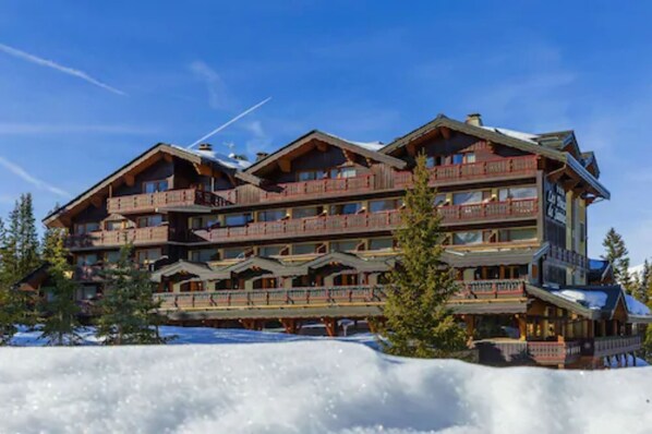 A multi-story lodge with balconies and a ski slope in the background. - Les Ducs de Savoie (Courchevel)