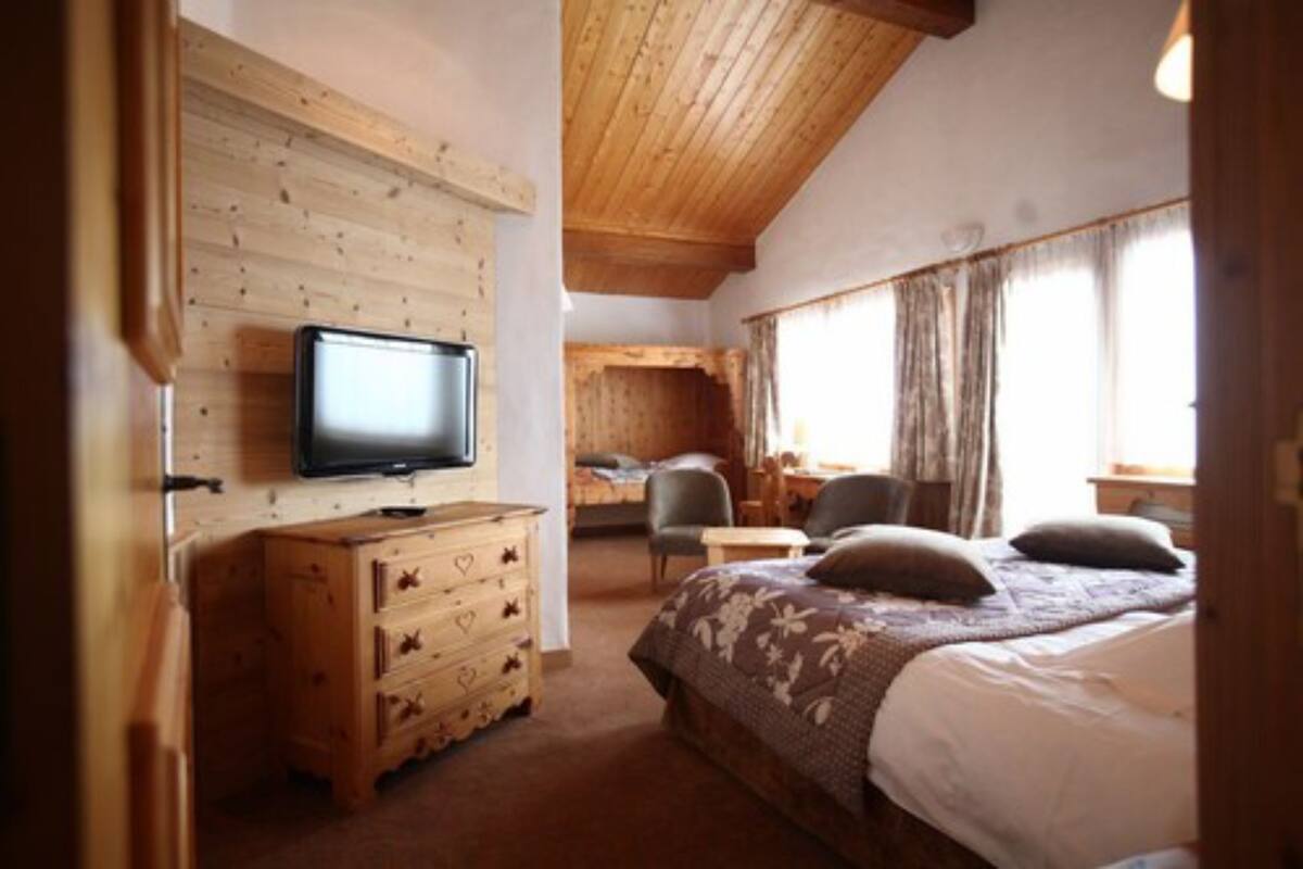 Une pièce chaleureuse avec une commode en bois, un lit recouvert d’une courtepointe à motifs floraux, un téléviseur et une fenêtre avec des rideaux.
