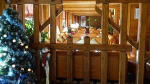 A cozy log cabin interior with a wooden dining area, a Christmas tree, and a fireplace.