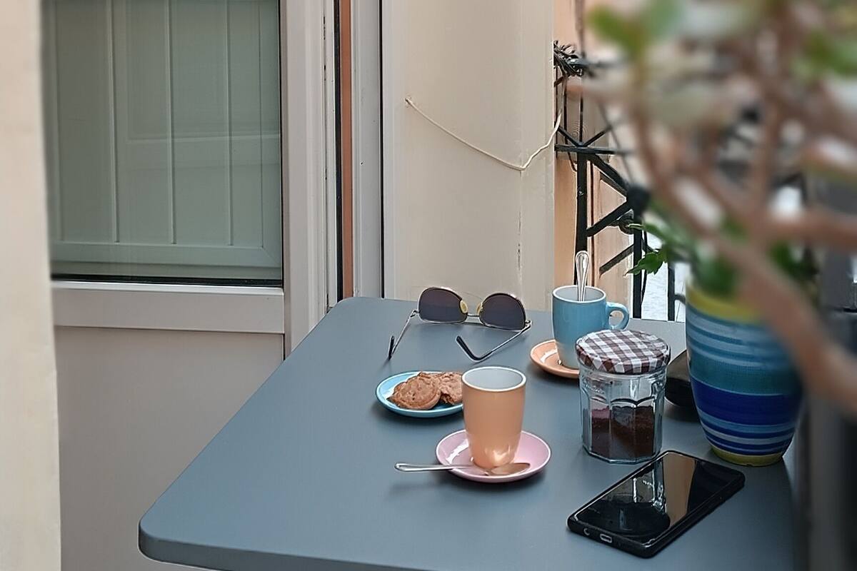 A small balcony with a table set for two, a door, and a potted plant.