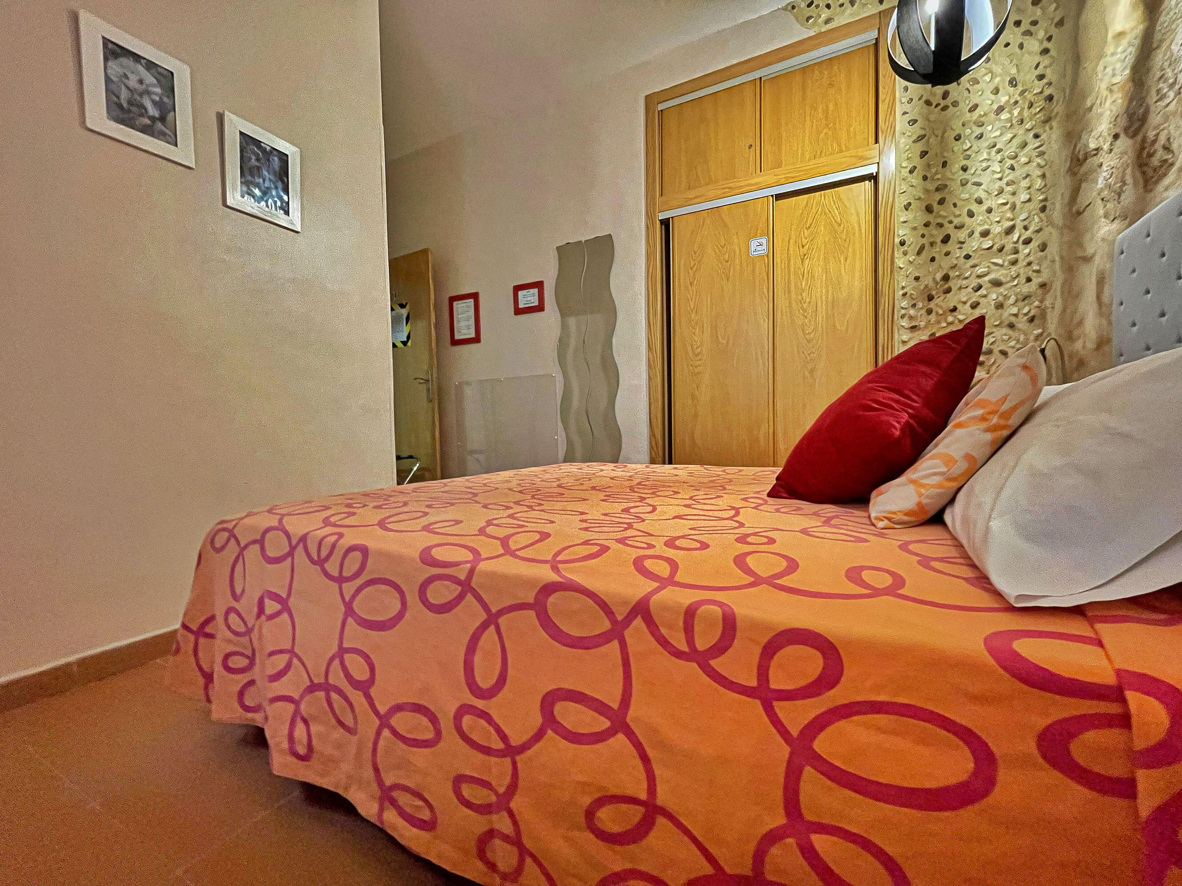A bedroom with a bed, pillows, a wooden wardrobe, and wall-mounted pictures.