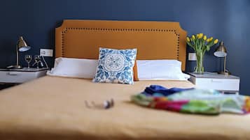 A neatly made bed with a brown headboard, white pillows, and a blue patterned pillow. There are two bedside tables with lamps and a vase of yellow flowers.