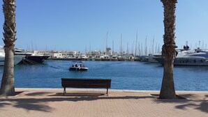 A marina with boats docked, a small boat in the water, and a bench in the foreground. - Alicante San Nicolás (Alicante)