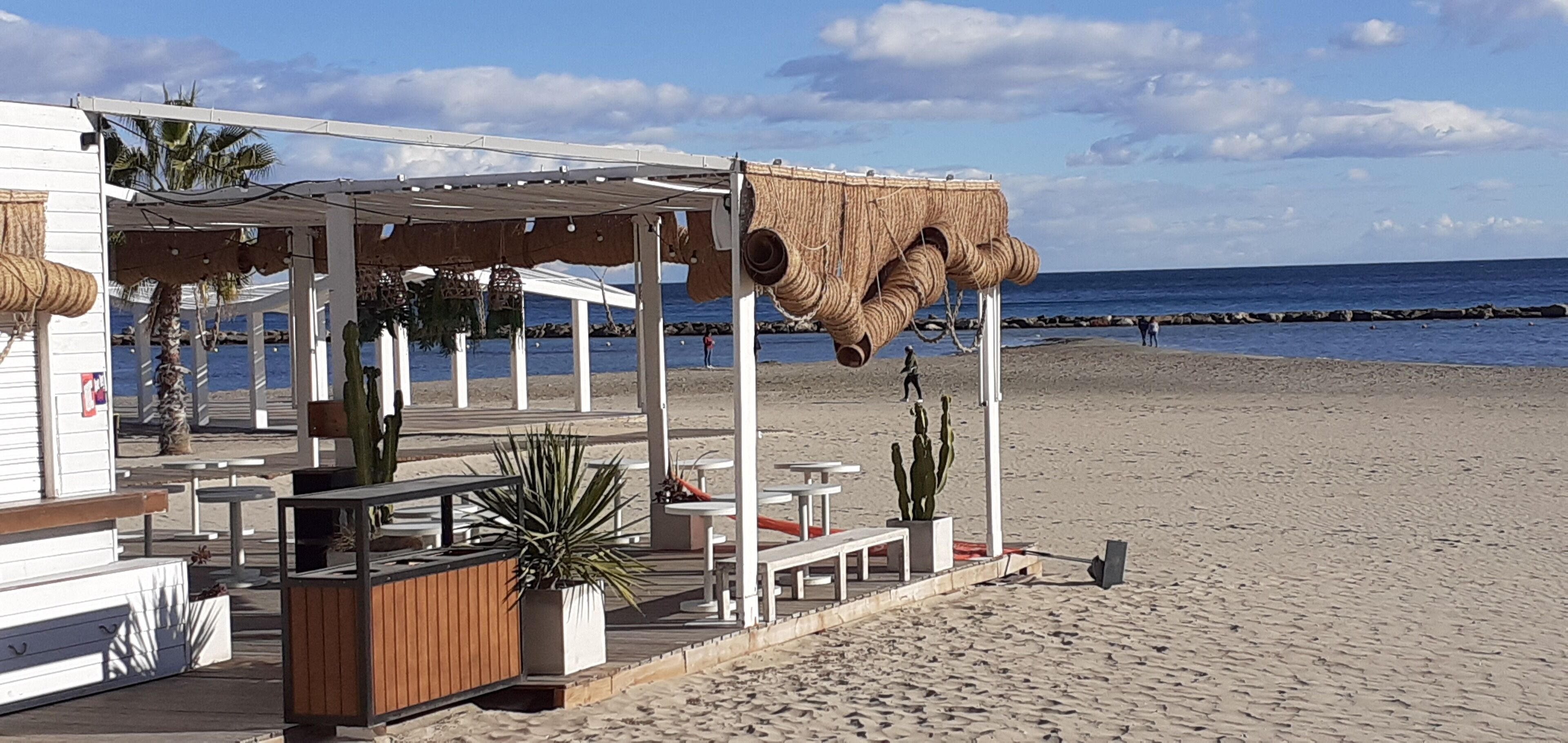 Un restaurante frente a la playa con terraza, techo de paja y vistas al mar.