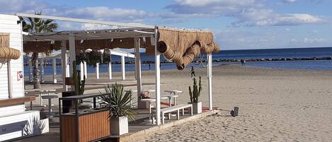 Un restaurante frente a la playa con terraza, techo de paja y vistas al mar.