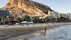 A beach with a rocky cliff in the background, a sandy shore, and buildings along the coastline. - Alicante San Nicolás (Alicante)