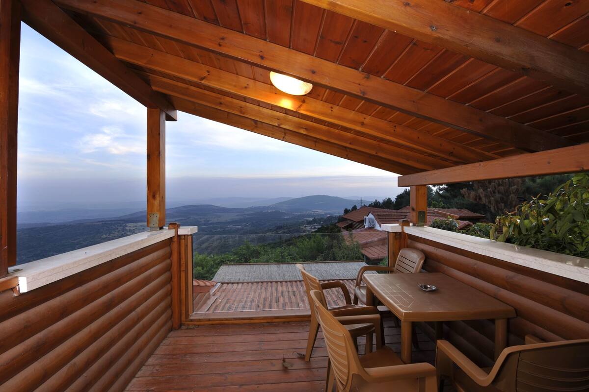 A wooden deck with a table and chairs, overlooking a mountainous landscape.