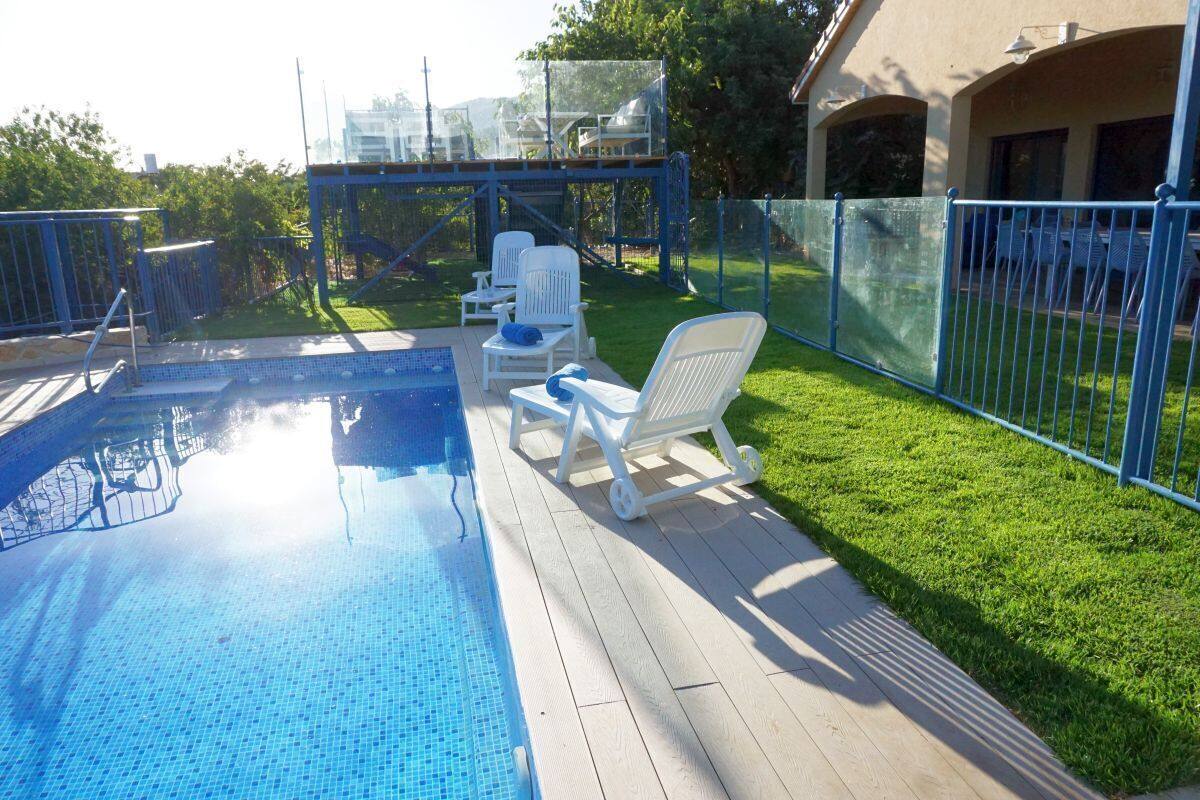A swimming pool with a tiled deck, surrounded by a blue fence, and white lounge chairs.