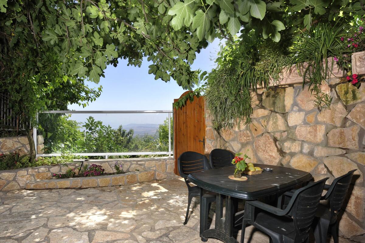 An outdoor patio with a stone wall, a wooden door, and a table with chairs.