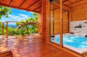 Una cabaña de madera con jacuzzi y una terraza de madera con vistas a un paisaje pintoresco.