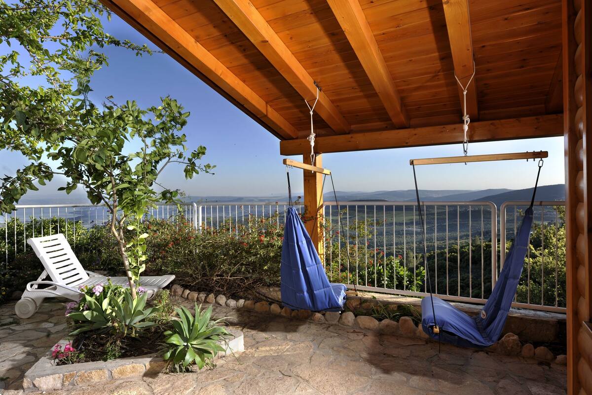 A wooden pergola with a swing chair and a hammock, overlooking a scenic landscape.