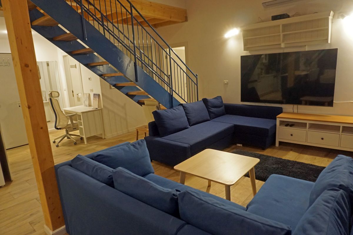 Un salón con un sofá seccional azul, una mesa de centro de madera, un televisor y una escalera.