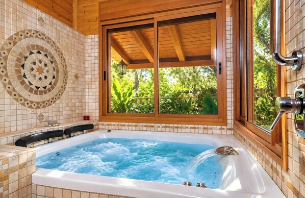 A spa room with a hot tub, wooden ceiling, and a window with a view of greenery.