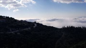 A mountainous landscape with a road winding through dense forests, leading to a distant view of a valley shrouded in clouds.