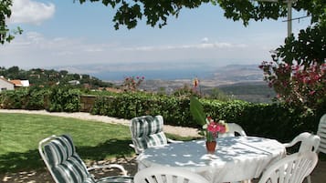 A patio with white chairs and a table, overlooking a scenic landscape.